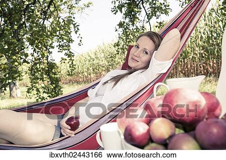 Stock Photograph - Pregnant woman in a hammock in the apple garden. Fotosearch