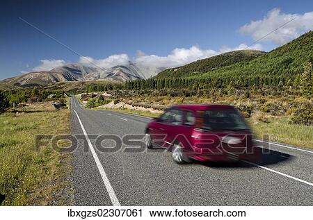Stock Image - "Red car driving on a country road, driving on the left, Arthur's Pass Road, South Island, New Zealand, Oceania". Fotosearch