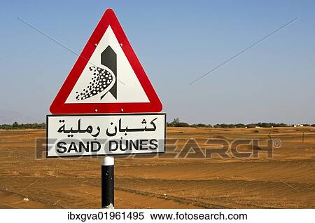 Stock Photography - "Road sign in English and Arabic warning of shifting sand dunes at a desert road, Sultanate of Oman, Middle East, Asia". Fotosearch