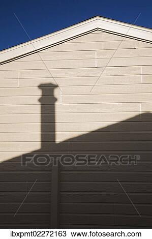 Stock Image - "Roofline and chimney shadow on the exterior side wall of a residential home, Quebec, Canada, North America". Fotosearch