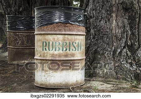 Stock Photography - "Rusty tin rubbish bin with word """"rubbish"""" next to a gnarled tree, New Zealand, Oceania". Fotosearch
