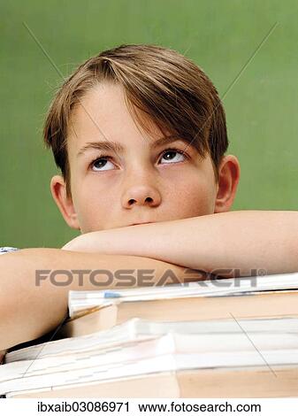 Stock Image - "Schoolboy in front of a school blackboard with a stack of books, looking frustrated, tired". Fotosearch