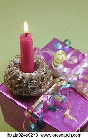 Stock Image - Small birthday cake with a candle on a birthday present. Fotosearch