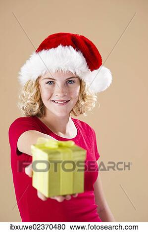 Smiling blond young woman wearing a Santa hat and presenting a gift View Large Photo Image Stock Image - Smiling blond young woman wearing a Santa hat and presenting a gift. Fotosearch