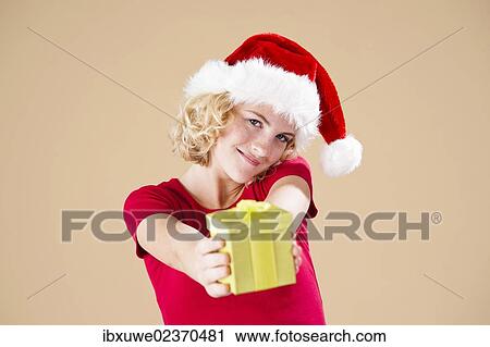 Smiling blond young woman wearing a Santa hat and presenting a gift View Large Photo Image Stock Image - Smiling blond young woman wearing a Santa hat and presenting a gift. Fotosearch