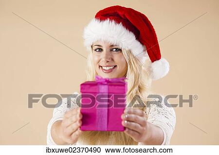 Smiling blond young woman wearing a Santa hat and presenting a gift View Large Photo Image Stock Image - Smiling blond young woman wearing a Santa hat and presenting a gift. Fotosearch