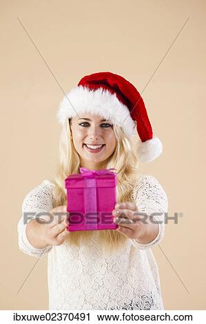 Smiling blond young woman wearing a Santa hat and presenting a gift View Large Photo Image Stock Image - Smiling blond young woman wearing a Santa hat and presenting a gift. Fotosearch