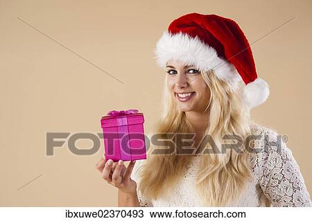 Smiling blond young woman wearing a Santa hat and presenting a gift View Large Photo Image Stock Image - Smiling blond young woman wearing a Santa hat and presenting a gift. Fotosearch