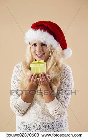 Smiling blond young woman wearing a Santa hat and presenting a gift View Large Photo Image Stock Image - Smiling blond young woman wearing a Santa hat and presenting a gift. Fotosearch