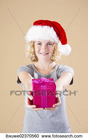Smiling blond young woman wearing a Santa hat and presenting a gift View Large Photo Image Stock Image - Smiling blond young woman wearing a Santa hat and presenting a gift. Fotosearch