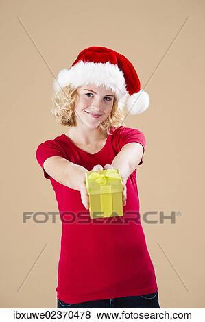Smiling blond young woman wearing a Santa hat and presenting a gift View Large Photo Image Stock Photo - Smiling blond young woman wearing a Santa hat and presenting a gift. Fotosearch