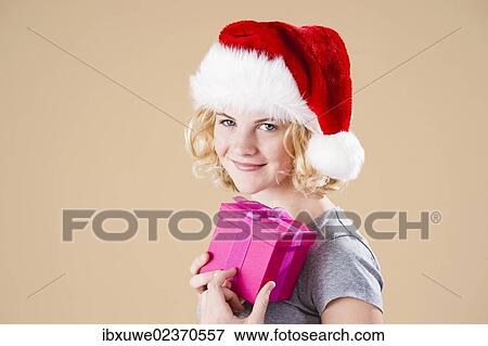 Smiling blond young woman wearing a Santa hat and presenting a gift View Large Photo Image Stock Photo - Smiling blond young woman wearing a Santa hat and presenting a gift. Fotosearch