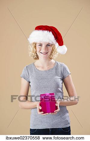Smiling blond young woman wearing a Santa hat and presenting a gift View Large Photo Image Stock Photo - Smiling blond young woman wearing a Santa hat and presenting a gift. Fotosearch