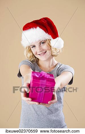 Stock Photo - Smiling blond young woman wearing a Santa hat and presenting a gift. Fotosearch
