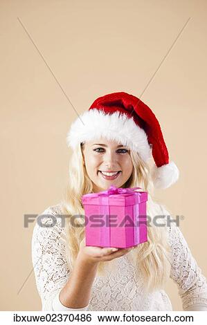 Stock Photograph - Smiling blond young woman wearing a Santa hat and presenting a gift. Fotosearch