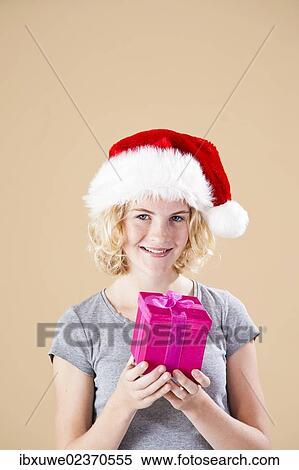 Stock Photography - Smiling blond young woman wearing a Santa hat and presenting a gift. Fotosearch