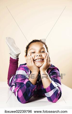 Smiling girl lying on her stomach with her hands supporting her head View Large Photo Image Stock Photograph - Smiling girl lying on her stomach with her hands supporting her head. Fotosearch