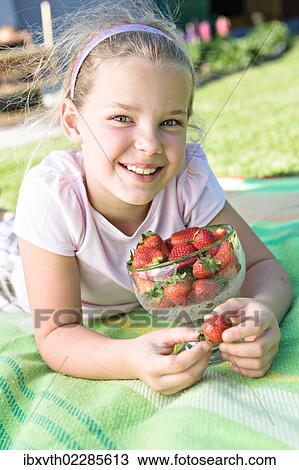 Stock Image - Smiling girl with strawberries in the garden. Fotosearch