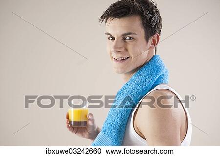 Stock Image - "Smiling young man after doing sport holding a glass of juice in his hand, Mannheim, Baden-Wurttemberg, Germany, Europe". Fotosearch