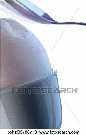 Stock Photo - Spoon is breaking the shell of an egg in an egg cup. Fotosearch