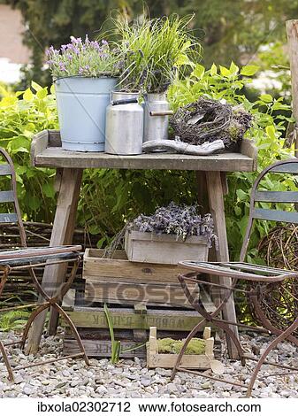 Stock Image - "Still life, decorative garden accessories, metal jugs on an old wooden table in a romantic garden". Fotosearch