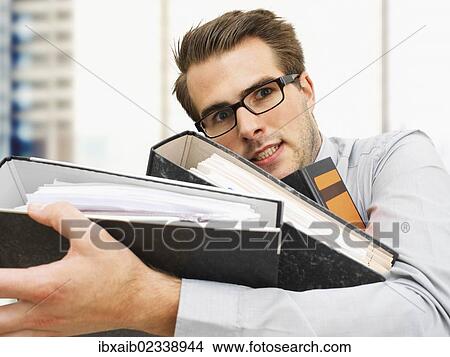 "Stressed young businessman wearing glasses carrying document files, serious face, overworked" View Large Photo Image Picture - "Stressed young businessman wearing glasses carrying document files, serious face, overworked". Fotosearch