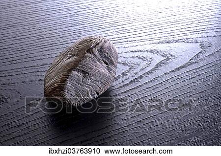 Stock Image - Structured stone lying on grained black wood. Fotosearch