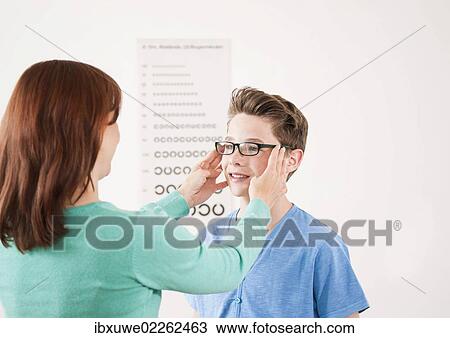 Stock Image - Teenage boy getting new glasses at the optician. Fotosearch
