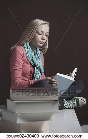 Stock Photo - "Teenage girl reading a book, with a pile of books at the front". Fotosearch