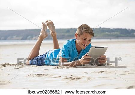Teenager lying with a digital tablet on a beach View Large Photo Image Stock Image - Teenager lying with a digital tablet on a beach. Fotosearch