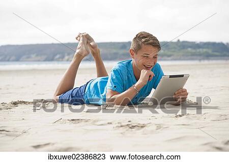 Teenager lying with a digital tablet on a beach View Large Photo Image Stock Image - Teenager lying with a digital tablet on a beach. Fotosearch