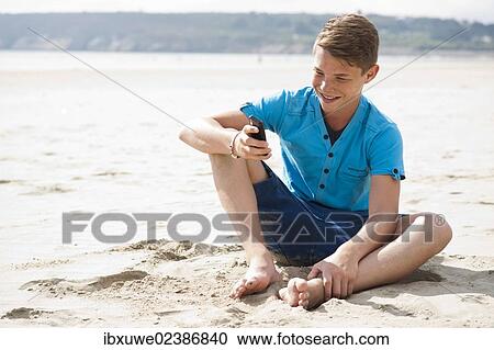 Teenager using his smartphone on a beach View Large Photo Image Stock Image - Teenager using his smartphone on a beach. Fotosearch