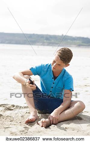 Stock Photo - Teenager using his smartphone on a beach. Fotosearch