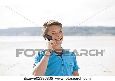 Teenager using his smartphone on a beach View Large Photo Image Stock Photography - Teenager using his smartphone on a beach. Fotosearch