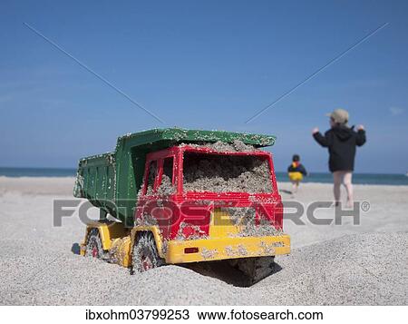 Stock Image - "Toy dumper truck on a beach, two children at the back, Mecklenburg-Western Pomerania, Germany, Europe". Fotosearch