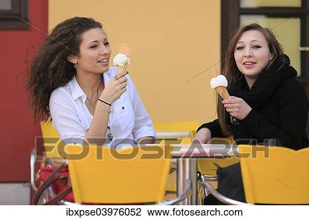 Stock Image - "Two girlfriends, teenagers, eating ice cream from cones on the terrace an ice cream parlour, Menton, Alpes-Maritimes, Provence-Alpes-Cote d'Azur, France, Europe". Fotosearch