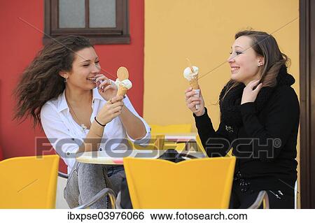 Stock Photograph - "Two girlfriends, teenagers, eating ice cream from cone on the terrace an ice cream parlour, Menton, Alpes-Maritimes, Provence-Alpes-Cote d'Azur, France, Europe". Fotosearch
