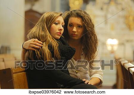 Stock Image - "Two girlfriends, teenagers, sitting in a church, one embracing the other, Menton, Alpes-Maritimes, Provence-Alpes-Cote d'Azur, France, Europe". Fotosearch