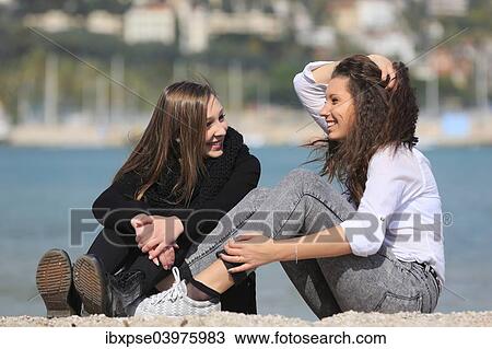 Stock Image - "Two girlfriends, teenagers, sitting on the beach, Menton, Alpes-Maritimes, Provence Alpes, France, Europe". Fotosearch