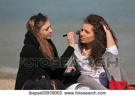 Stock Image - "Two girlfriends, teenagers, sitting on the beach, applying makeup on each other, Menton, Alpes-Maritimes, Provence Alpes, France, Europe". Fotosearch