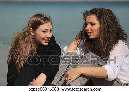 Stock Photo - "Two girlfriends, teenagers sitting on the beach, Menton, Alpes-Maritimes, Provence Alpes, France, Europe". Fotosearch