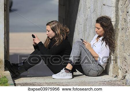 "Two girlfriends, teenagers, sitting on the floor, leaning against a wall and writing text message on their mobile phones, Menton, Provence-Alpes-Cote d'Azur, France, Europe" View Large Photo Image Stock Photograph - "Two girlfriends, teenagers, sitting on the floor, leaning against a wall and writing text message on their mobile phones, Menton, Provence-Alpes-Cote d'Azur, France, Europe". Fotosearch