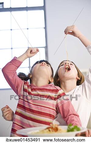 Stock Image - Two girls eating spaghetti together. Fotosearch