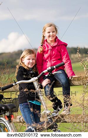 Stock Image - Two girls with bicycles in rural landscape. Fotosearch