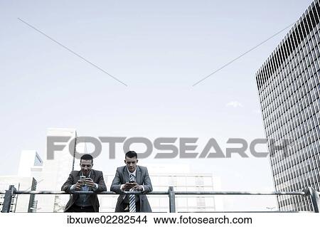 Two managers checking their smartphones during a break View Large Photo Image Picture - Two managers checking their smartphones during a break. Fotosearch