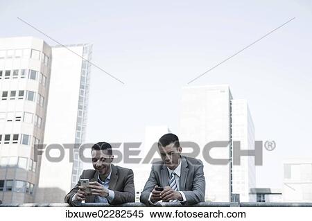 Two managers checking their smartphones during a break View Large Photo Image Stock Photography - Two managers checking their smartphones during a break. Fotosearch