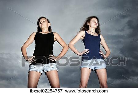 Stock Photo - "Two self-confident teenage girls standing in front of storm clouds looking into the distance, symbolic image, youth looking into the future". Fotosearch