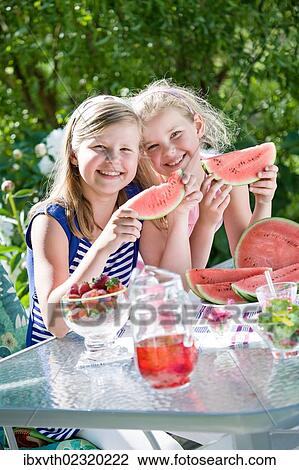Stock Image - Two sisters eating watermelon in the garden. Fotosearch