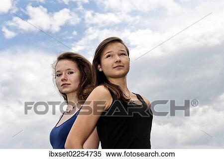 Two teenage girls standing back to back in front of cloudy sky View Large Photo Image Stock Photography - Two teenage girls standing back to back in front of cloudy sky. Fotosearch