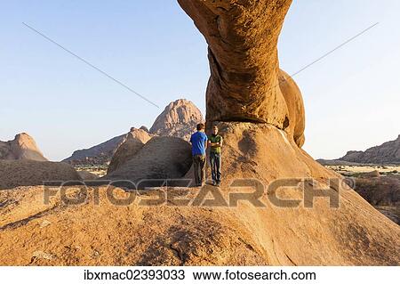 "Two young men standing under a arch rock, near the Spitzkoppe granite peaks, Damaraland, Namibia, Africa" View Large Photo Image Stock Image - "Two young men standing under a arch rock, near the Spitzkoppe granite peaks, Damaraland, Namibia, Africa". Fotosearch
